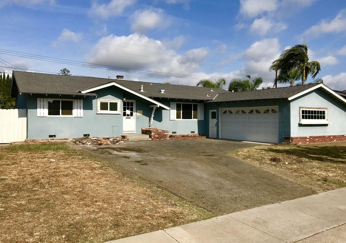 A tired single-storey Orange County ranch house with a dry lawn and debris by the porch