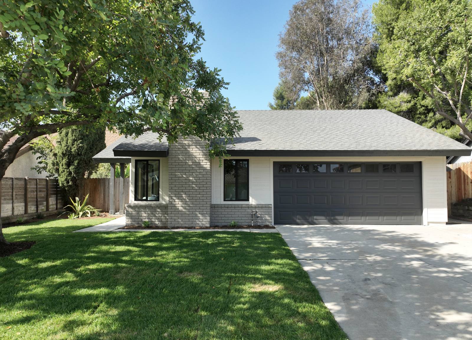The same view after: trees cut back, new lawn, painted brick, a dark garage door and new windows.