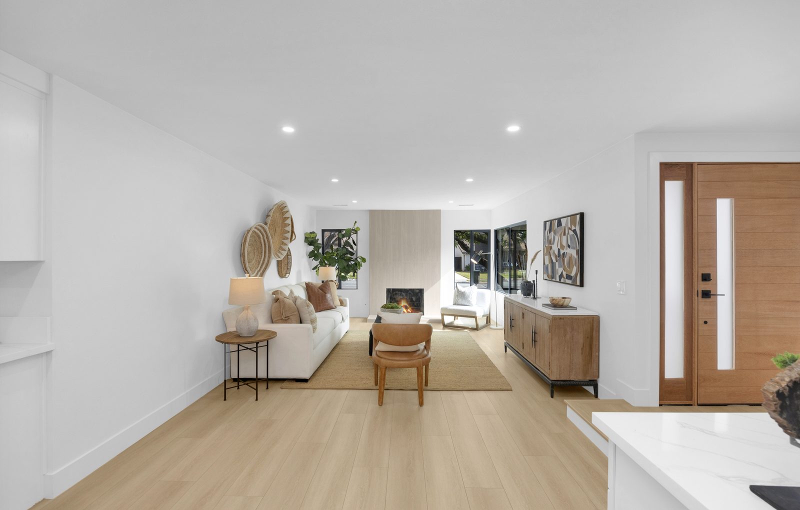 The same room finished: pale wood floors, white walls, a tiled fireplace in the same position and the same windows either side of it.